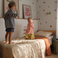 Two children jumping on a bed in a kids bedroom featuring the cuddle collective organic cotton bedding. The bed has cream bedding with red star patterns and a stripe sheet set