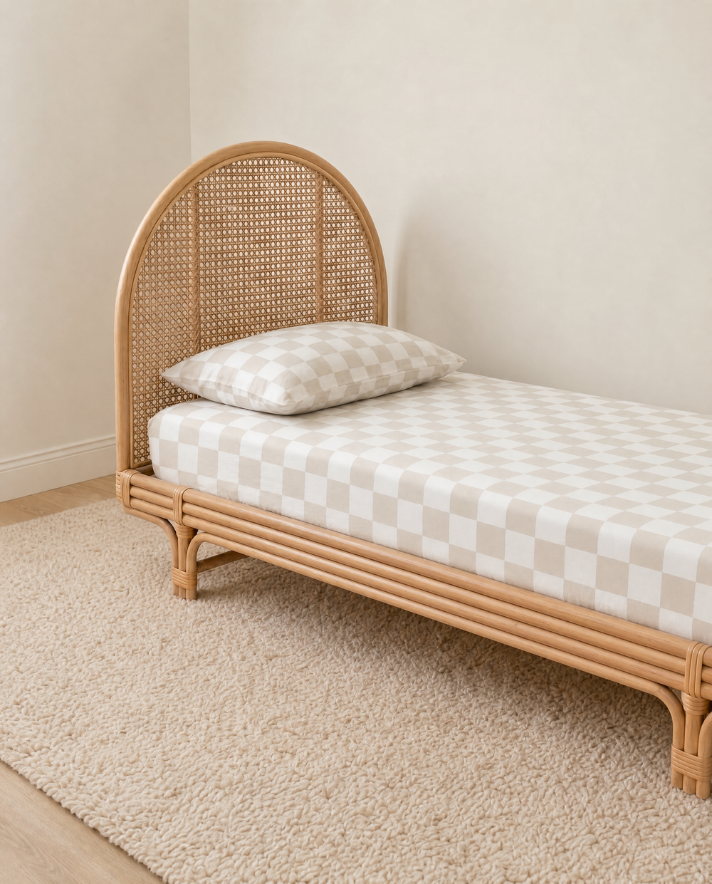 beige and white checkered organic cotton fitted sheet and pillow on a textured cream rug against a neutral beige wall.