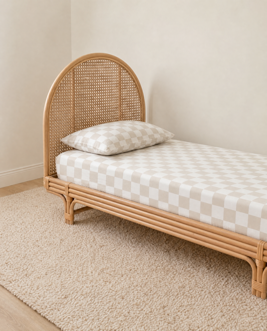 beige and white checkered organic cotton fitted sheet and pillow on a textured cream rug against a neutral beige wall.