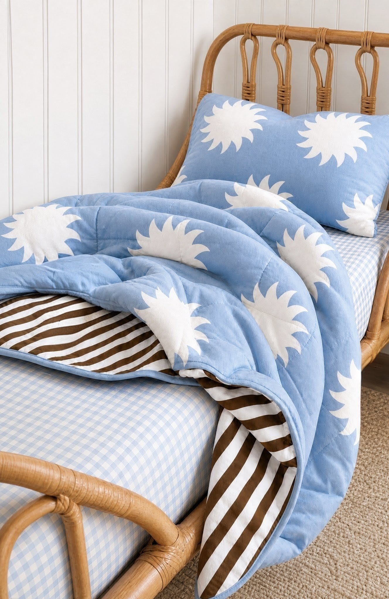 Blue reversible quilt with white star patterns and chocolate brown stripes on a kids bed with a wooden headboard 