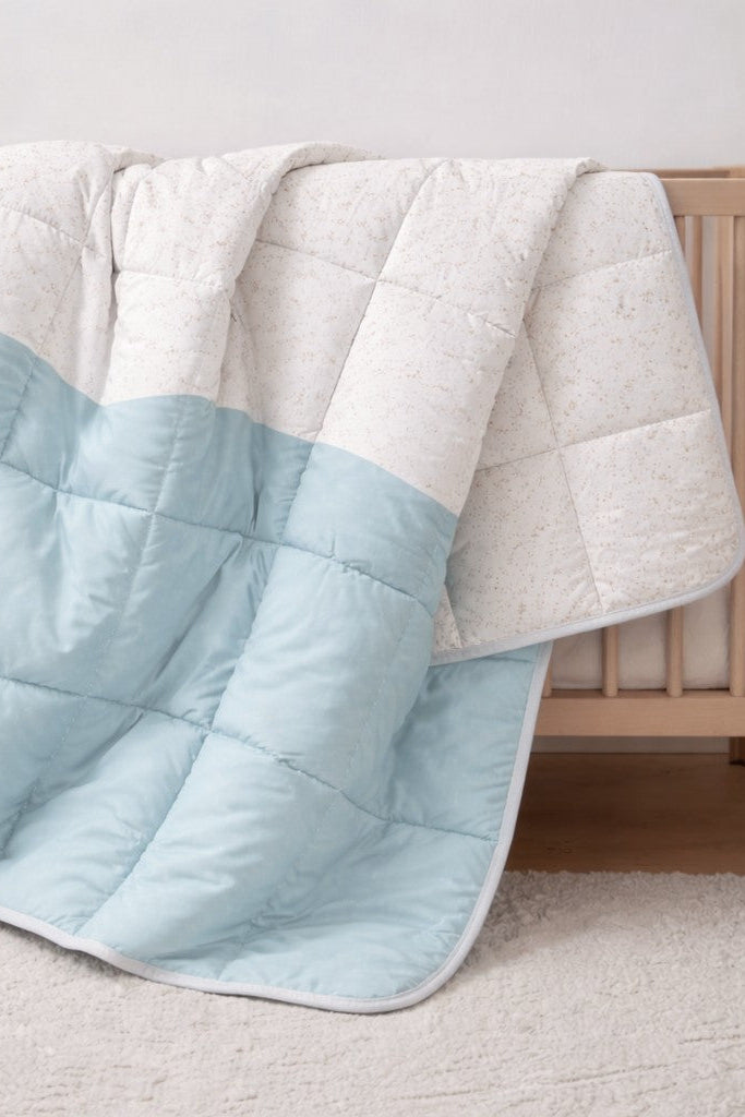 Baby blue wave and speckle reversible quilt hanging on a bed in a kids bedroom